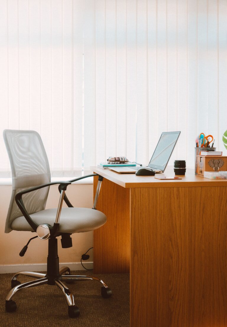 Silla ergonómica de oficina junto a escritorio de madera en home office con luz natural